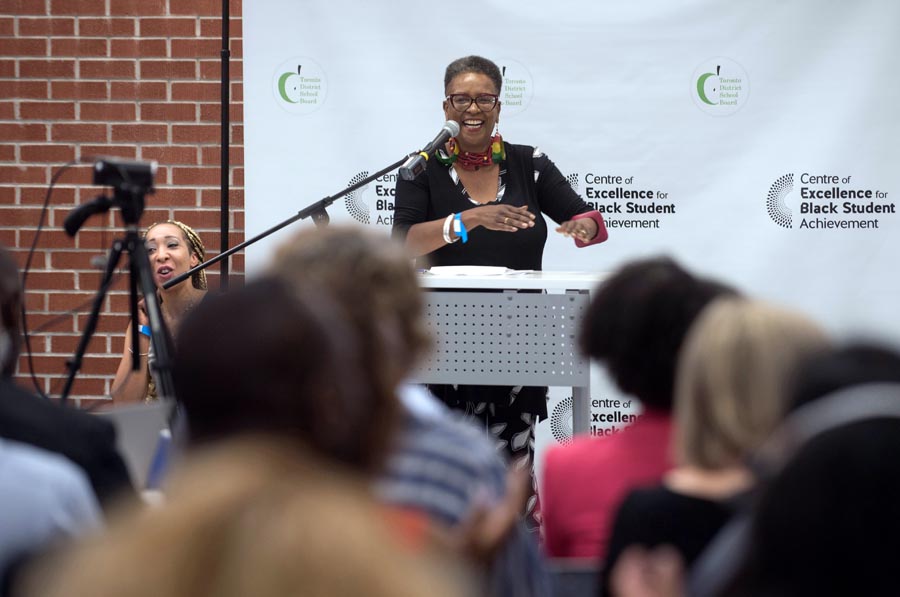 Host Itah Sadu smiling at the podium. Open Gallery